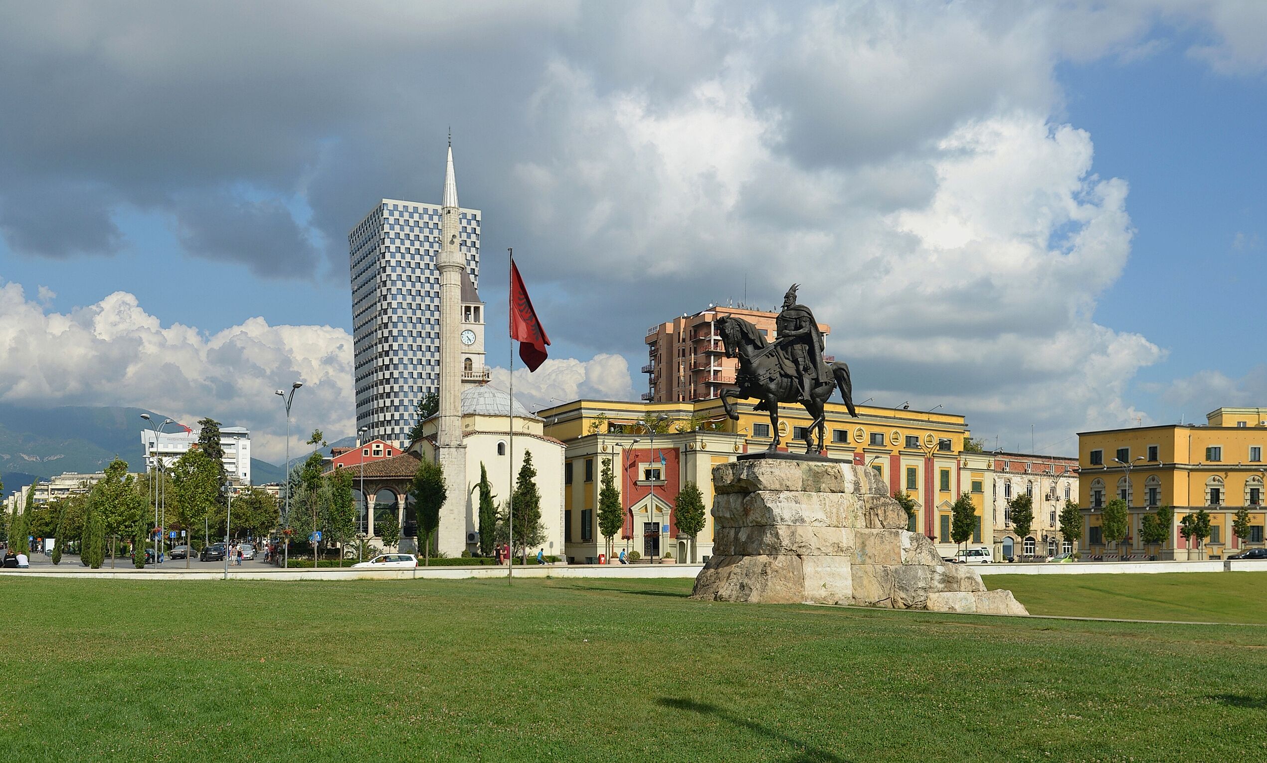Eine Statue auf einem Sockel in einem Park, im Hintergrund sind Gebäude zu sehen.
