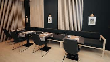 Un comedor moderno con una mesa larga, sillas negras y un banco. Hay cuadros en la pared y una lámpara colgante sobre la mesa.