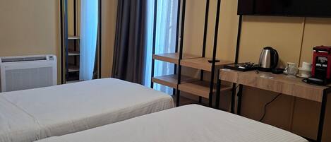 A hotel room with two beds, a desk with a TV, a kettle, and a coffee maker.