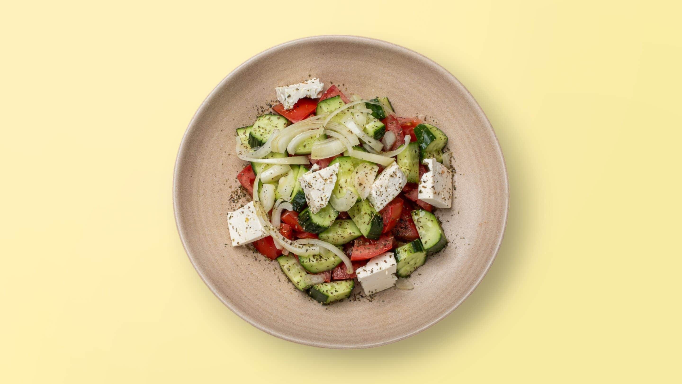 A plate of Greek salad with cucumbers, tomatoes, onions, and feta cheese.