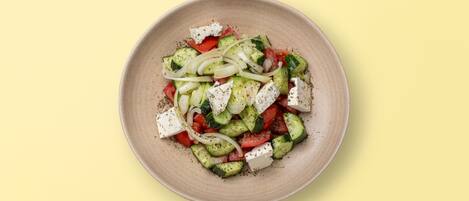 A plate of Greek salad with cucumbers, tomatoes, onions, and feta cheese.