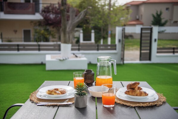 A breakfast table with croissants, juice, and a pitcher on a wooden table outdoors. - Alios Gaia (Sithonia)