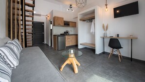 A modern living space with a sofa, a glass-top coffee table, a dining area with a chair, a kitchen with wooden cabinets, and a TV mounted on the wall. - Alios Gaia (Sithonia)