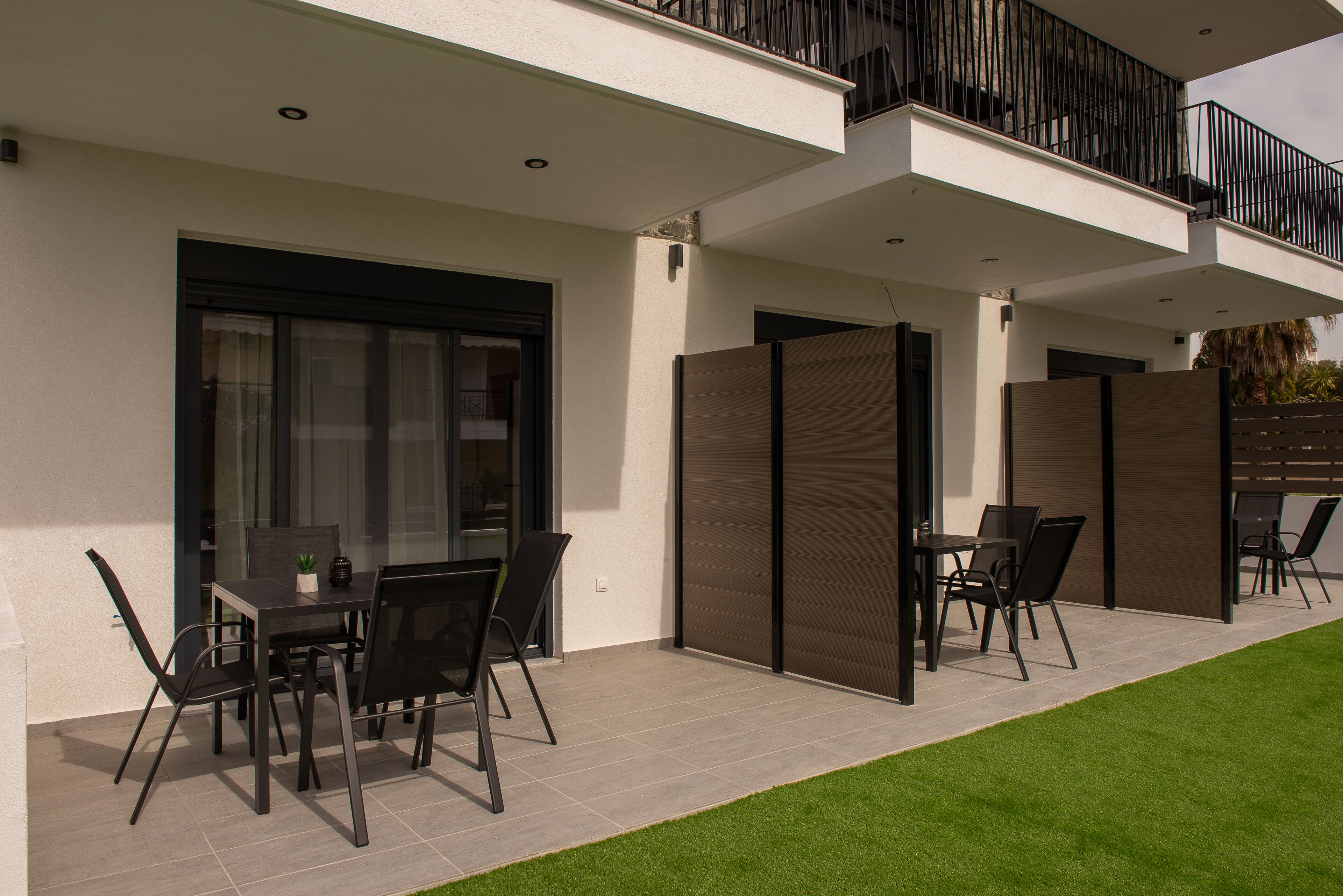 Un patio moderno al aire libre con una mesa de comedor y sillas, una puerta corrediza de vidrio y un balcón con barandilla negra.