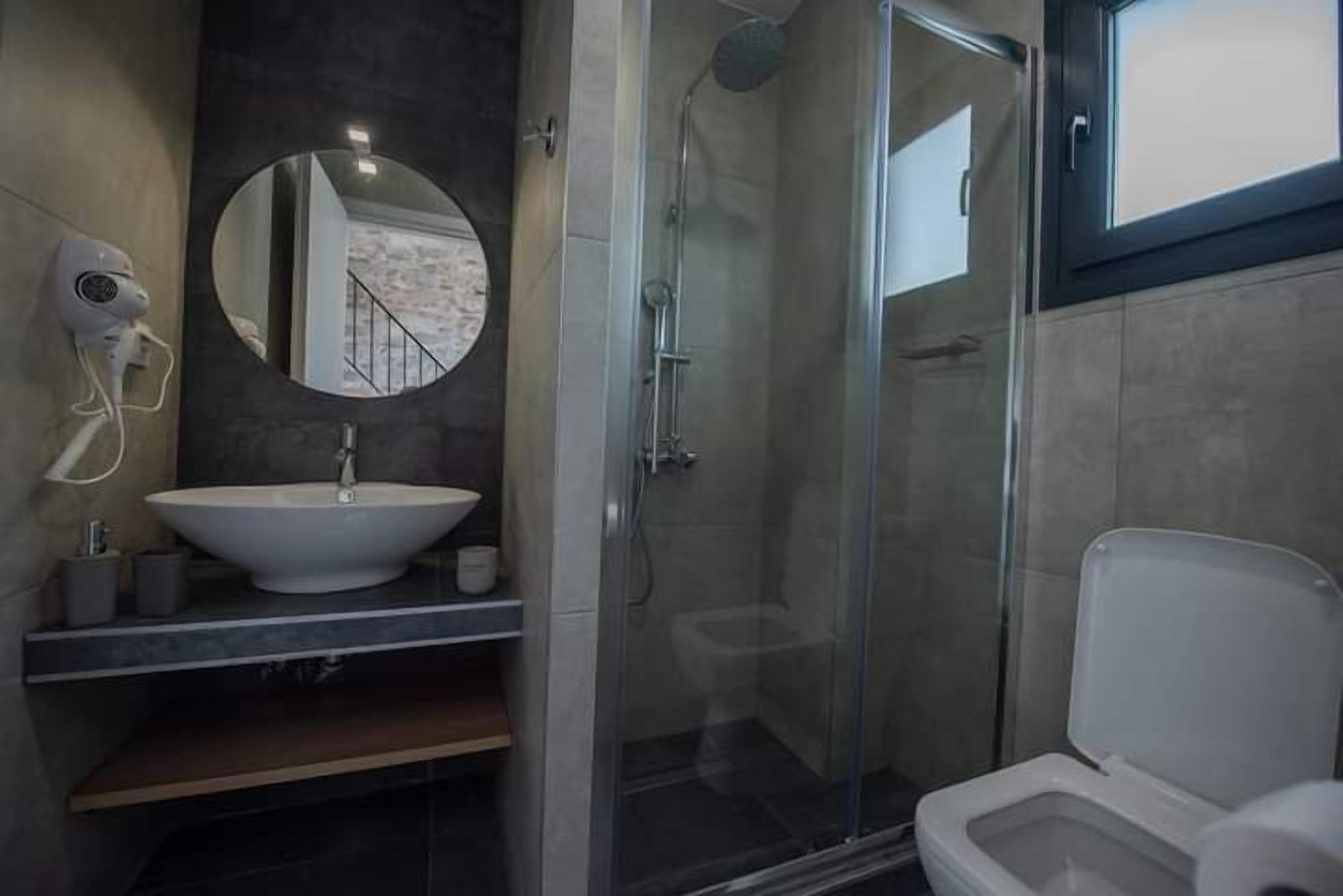 Une salle de bain moderne dotée d’un grand lavabo, d’un miroir, d’un sèche-cheveux et d’une douche à parois de verre.