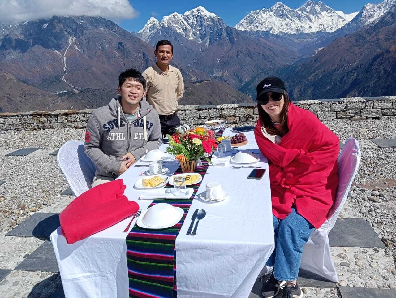 Mesa al aire libre con montañas de fondo, mostrando una comida y un jarrón con flores.