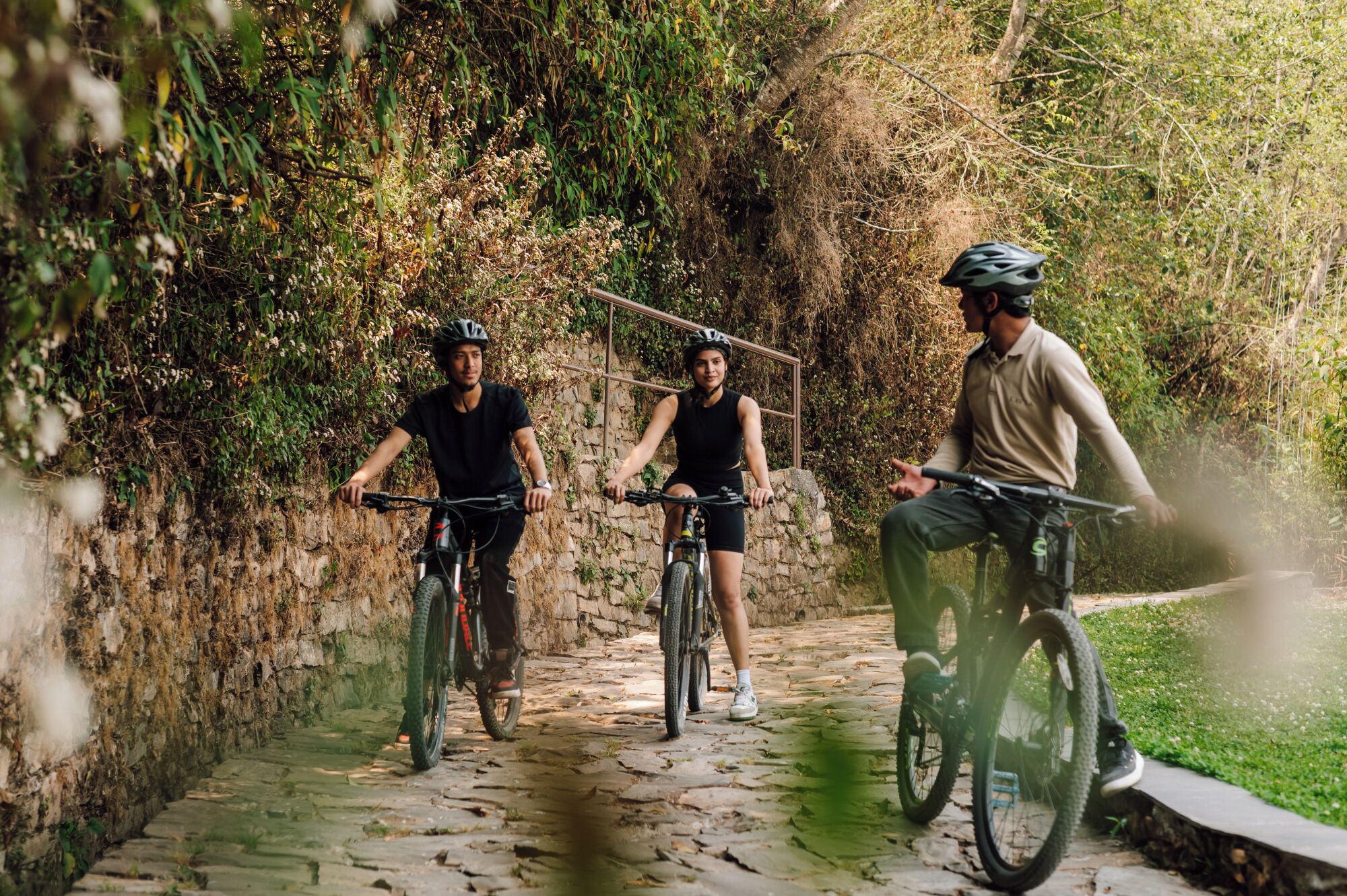 Three cyclists on a cobblestone path surrounded by greenery.
