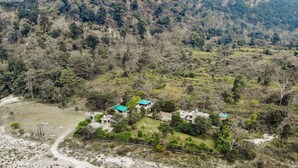 An aerial view of a small cluster of buildings with green roofs, surrounded by a forested area with a dirt path leading to them. - 1B-Wild Heritage-102 N By bnbmehomes (Salt)