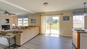 Un salón espacioso con un sofá seccional beige grande, un ventilador de techo y un suelo de vidrio corredera que da a un patio.