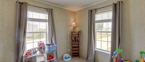 A child's playroom with a window, a bookshelf, a toy train, and a play mat.