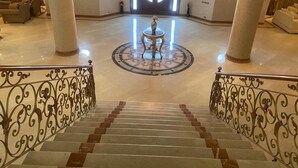 Un vaste hall d’entrée avec un lustre central, une table ronde et un escalier agrémenté de rampes décoratives.