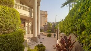 Un espace extérieur bien entretenu, avec un chemin menant à un bâtiment à l’architecture classique, doté de colonnes et d’un balcon.