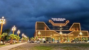 The exterior of the St. Vegas Hotel with a modern architectural design, featuring a prominent entrance and a parking area with several cars. - ST Vegas Hotel (Hadxayfong)