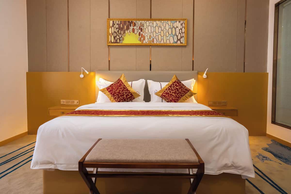 A hotel room with a large bed, two bedside lamps, a bench, and a wall-mounted artwork.