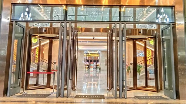 A modern hotel entrance with a revolving door, glass panels, and a visible interior with a staircase and plants. - ST Vegas Hotel (Hadxayfong)