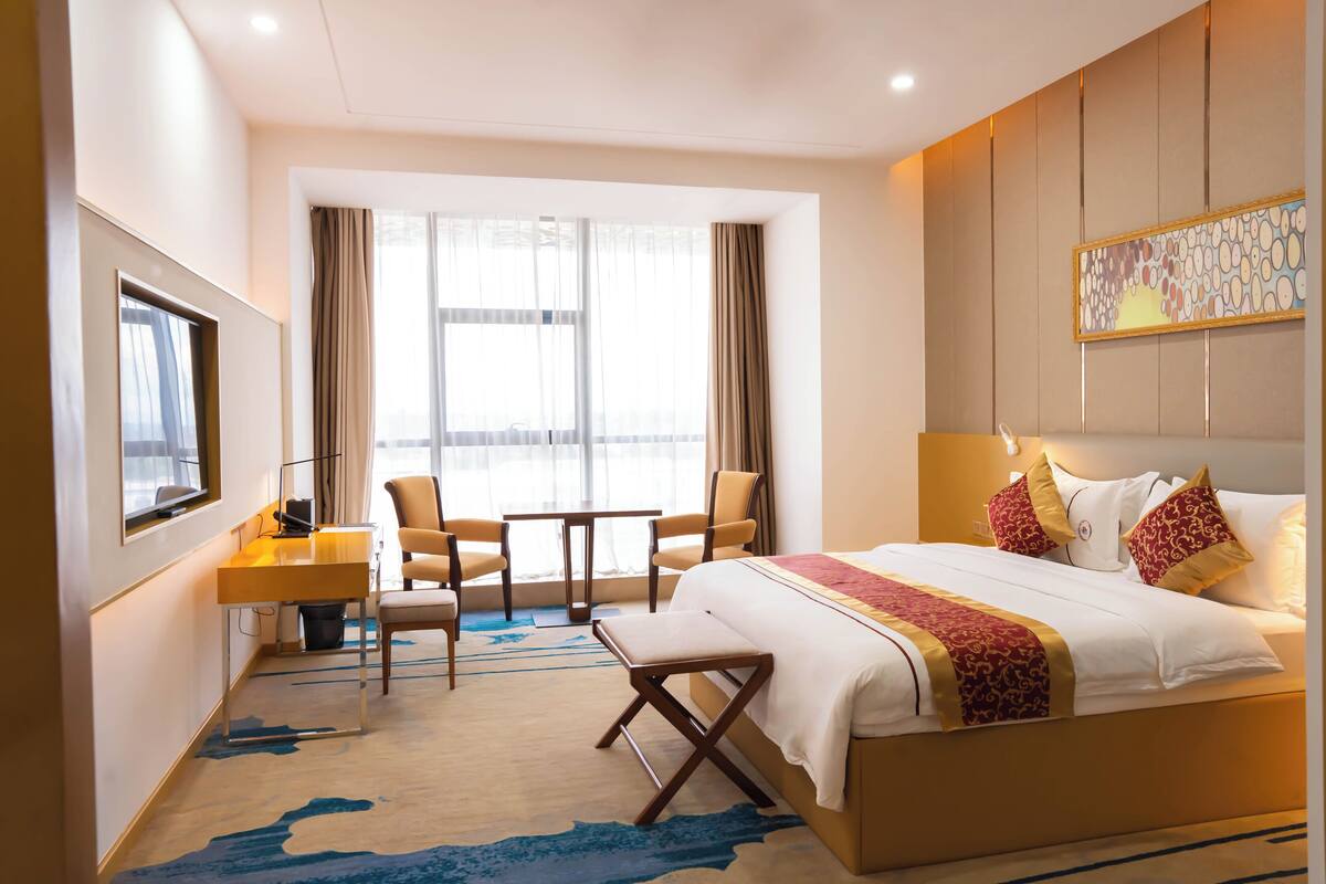 A hotel room with a bed, desk, chairs, and a large window.