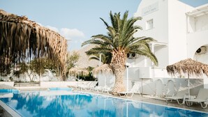 A pool area with lounge chairs, palm trees, and a white building with the sign "ASPRO PHOS". - Aspro Phos (Santorini)