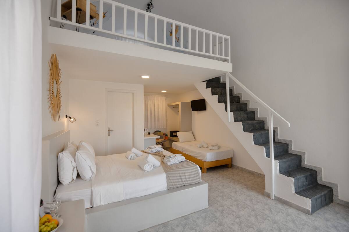A modern hotel room with a lofted sleeping area, a staircase, and a small seating area with a table and chairs.
