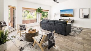 Un salon spacieux avec un canapé gris, une table basse en bois et une grande fenêtre donnant sur un paysage verdoyant.