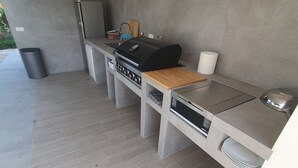Una cocina al aire libre moderna con una parrilla empotrada, un lavamanos y una encimera.