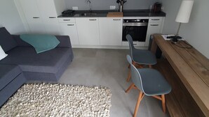 Un espacio habitable compacto con kitchenette, un sofá, dos sillas y un banco de madera.