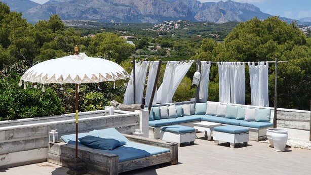 Una terraza en la azotea con una cama de madera, un sofá y una sombrilla.