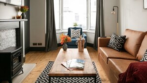 A living room with a fireplace, a sofa, a coffee table, and a view through a bay window. - Sutton House by Pureserviced (Plymouth)