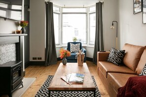 A living room with a fireplace, a sofa, a coffee table, and a view through a bay window. - Sutton House by Pureserviced (Plymouth)