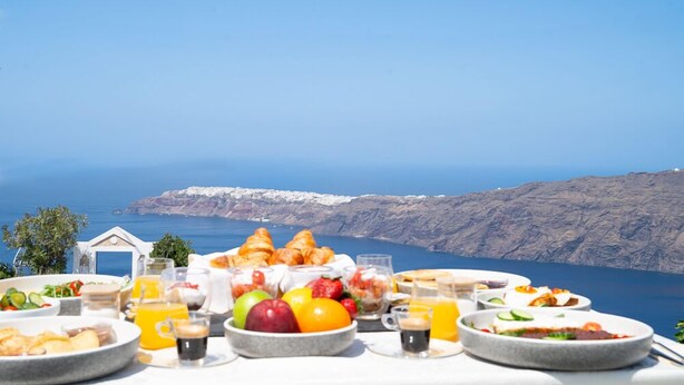 Una mesa de desayuno con diversos platos y bebidas, con vistas a una costa pintoresca con acantilados y el mar.