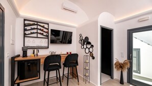 Una cocina moderna con lavavajillas integrado, encimera de madera, dos taburetes negros, televisor montado en la pared y una estantería para vinos.