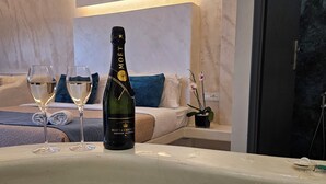 Un minibar con una botella de champán Moët y dos copas de vino, una bañera, y una cama con almohadas y una manta azul.