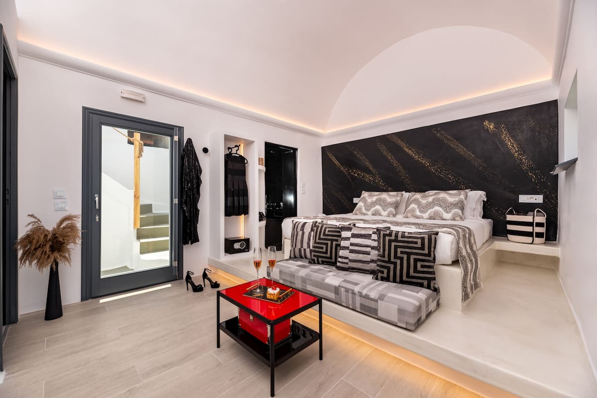 Un dormitorio moderno con una cama, un sofá, una mesa roja y un ventanal grande.