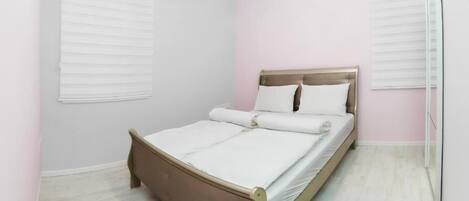 Un dormitorio con cama, paredes blancas y suelo de color claro.