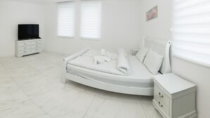 A bedroom with a bed, a TV, a dresser, and two windows with blinds.
