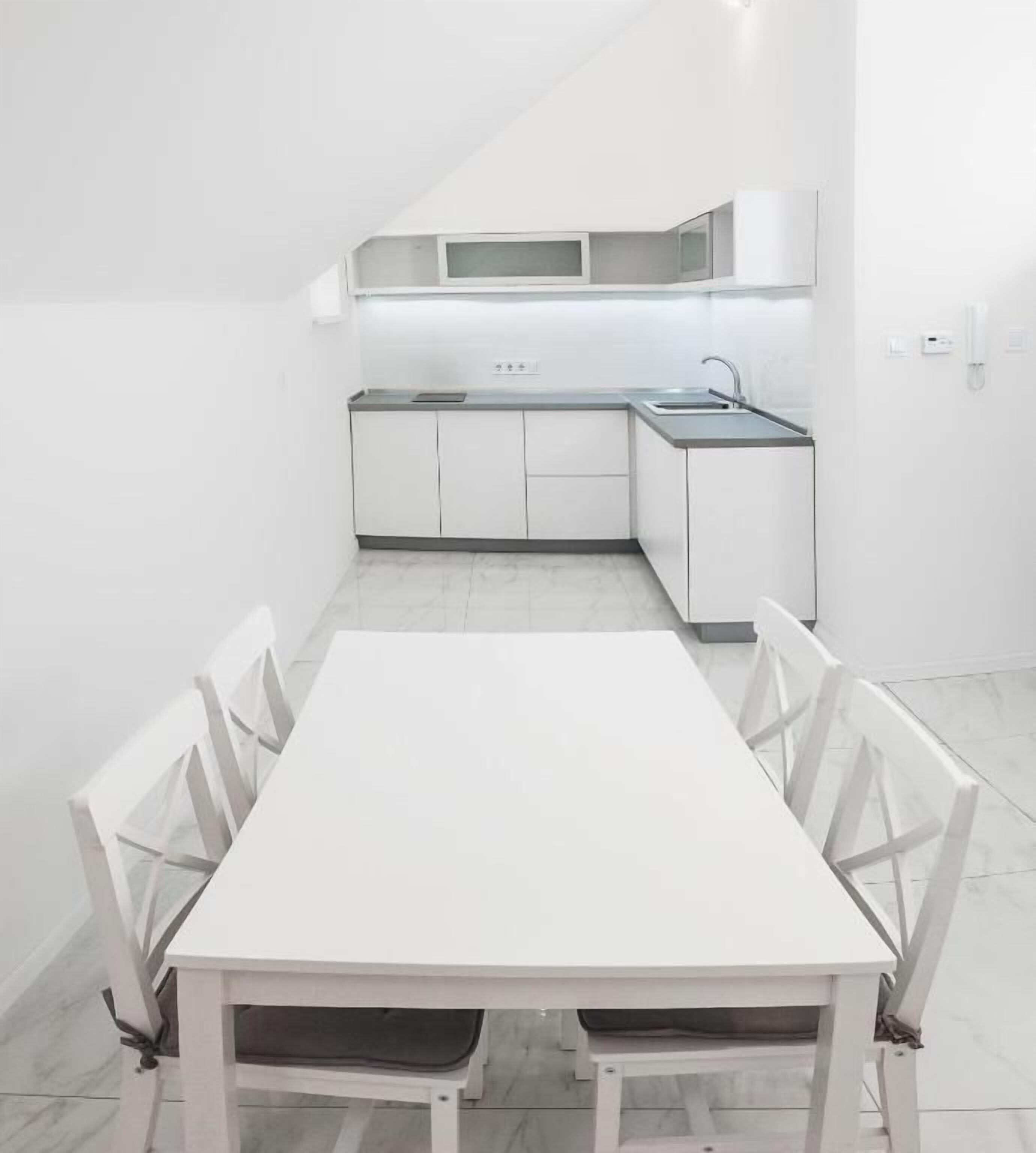 A compact kitchen with white cabinetry, a sink, and a dining area with a table and chairs.