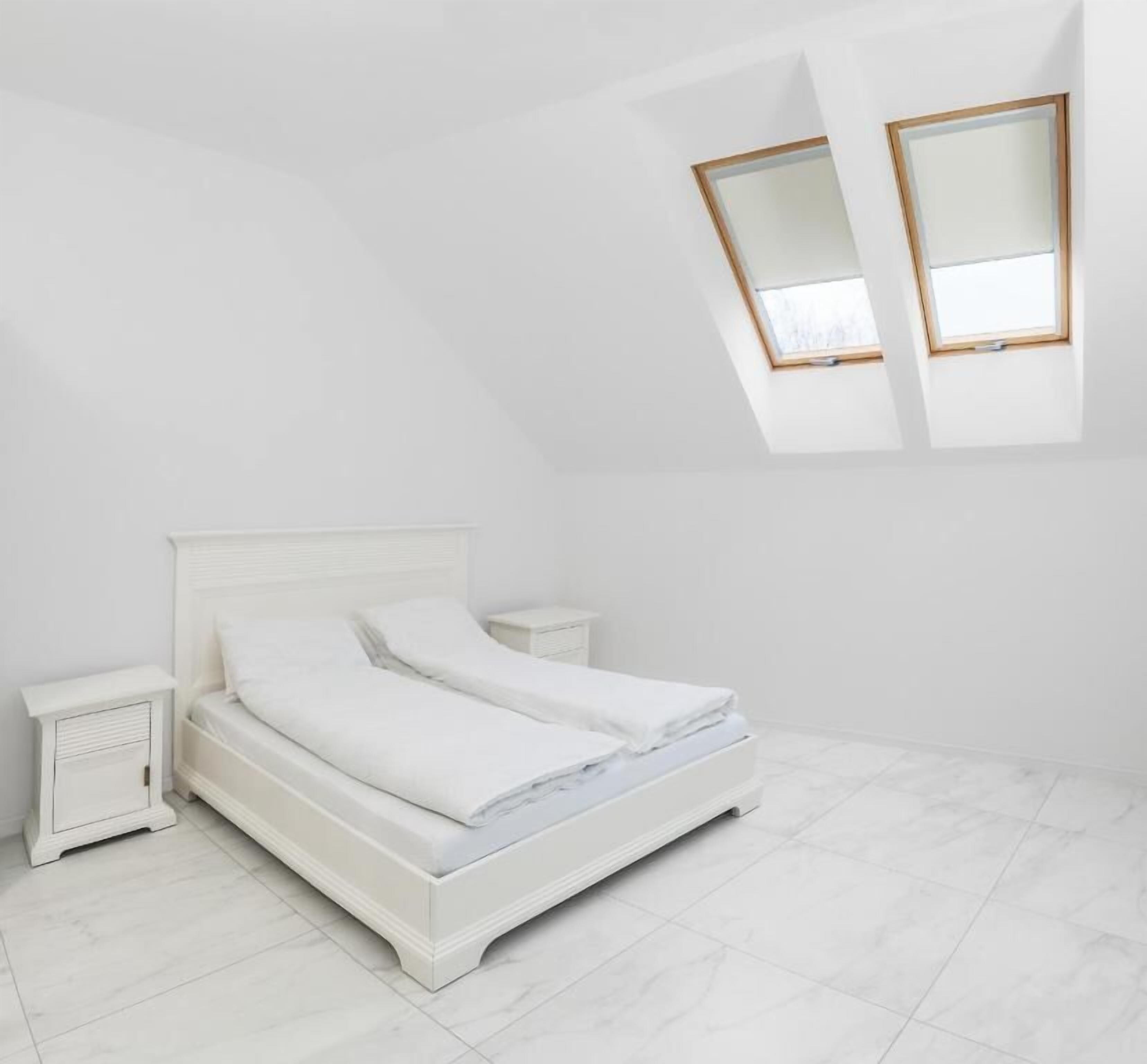 Un dormitorio blanco con cama, mesitas de noche y tragaluz.