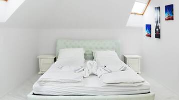 Cama bem arrumada com lençóis e almofadas brancas, cabeceira estofada em verde claro e duas mesas de cabeceira com mesinhas de apoio brancas.