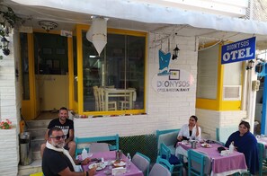An outdoor dining area with tables and chairs, a sign for 'Dionysos Hotel & Restaurant', and a yellow door.