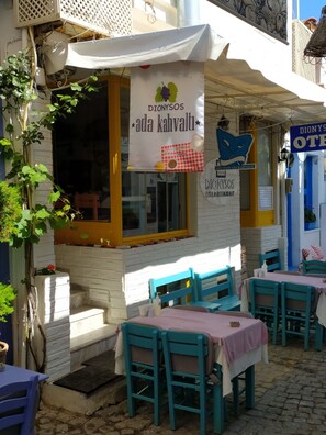 An outdoor seating area with tables and chairs, a banner advertising 'Dionysos ada kahvalti', and a blue awning.
