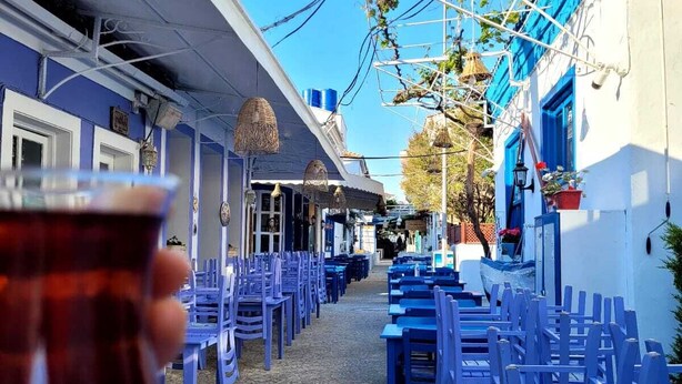 Une rue étroite, avec des chaises et des tables bleues, ce qui laisse supposer qu’il s’agit d’un café ou d’un restaurant.