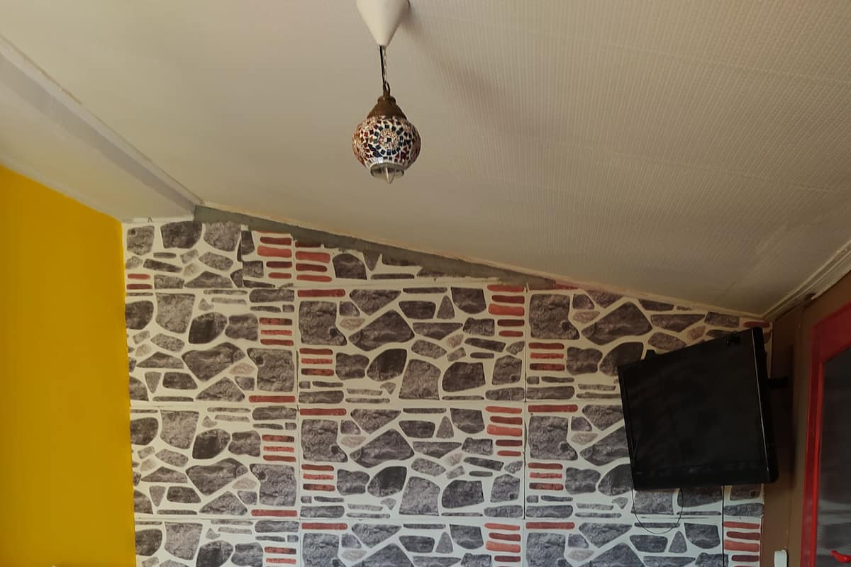 A room with a stone-patterned wall, a bed with white linens, a red chair, and a television mounted on the wall.
