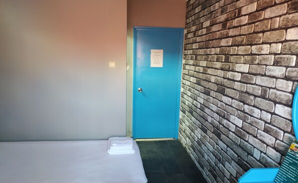 A small room with a single bed, a blue door, and a brick wall. - Dionysos Otel & Restoran & Ada Kahvaltı (Bozcaada)