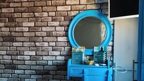 Une pièce avec un mur en briques, une commode bleue avec un miroir, un lit avec du linge de maison blanc et une petite table avec un panier.