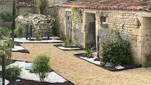Un edificio de piedra con tejado de baldosas, una pared de piedra y un jardín con plantas y un sendero.