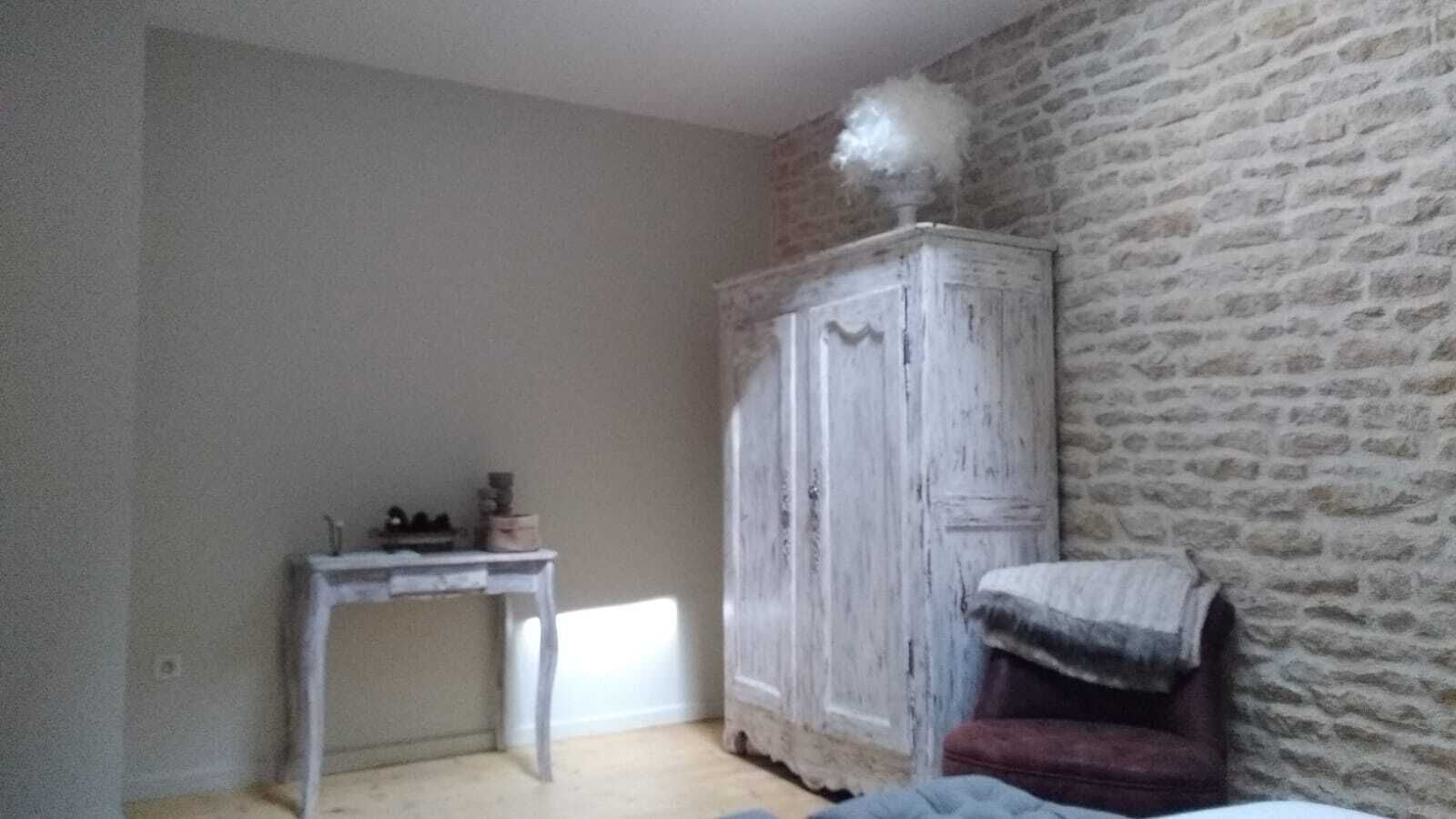 Una habitación con un escritorio blanco, un armario y una pared de piedra.