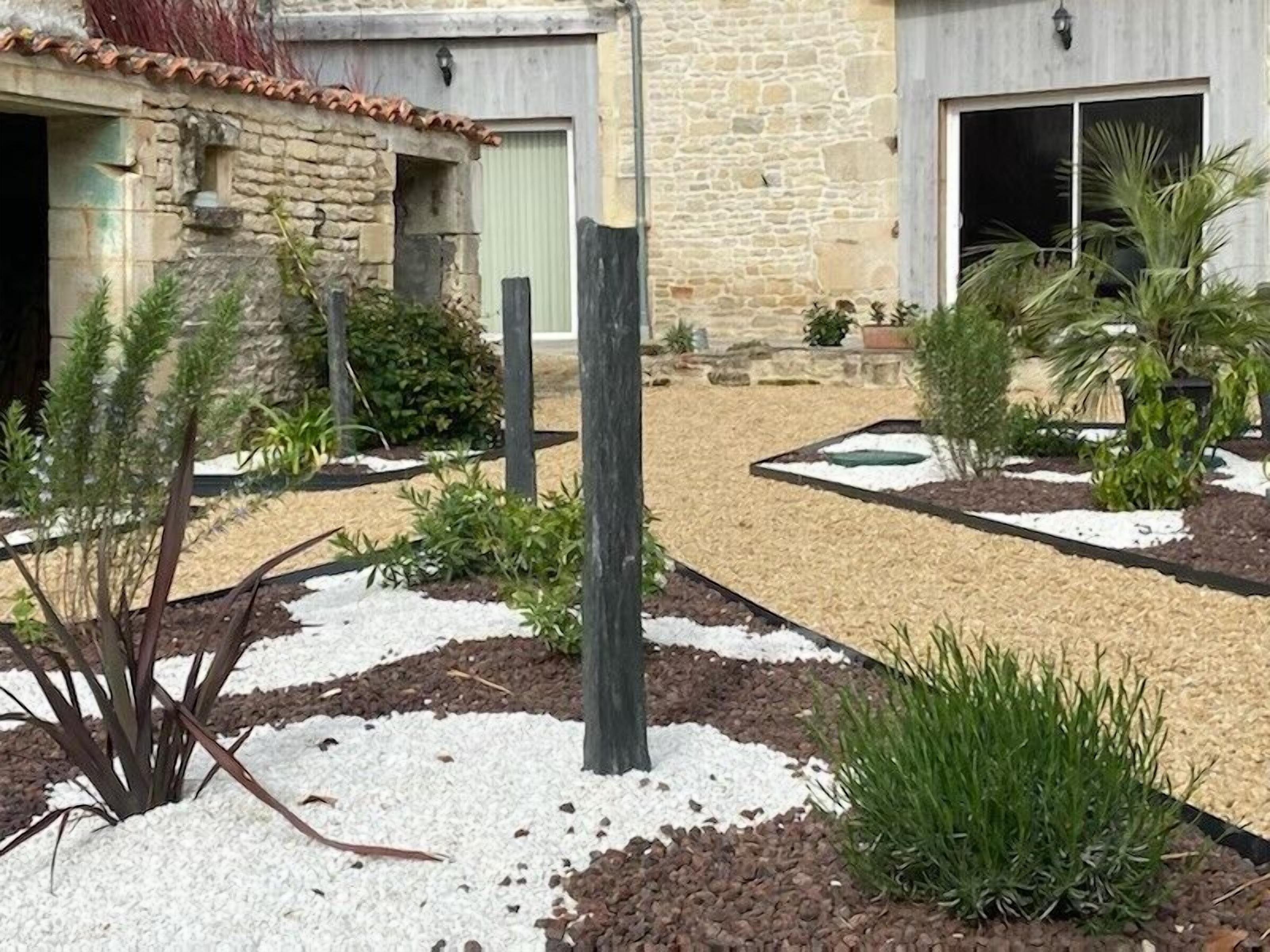 A courtyard with a stone building, a wooden pergola, and various plants.
