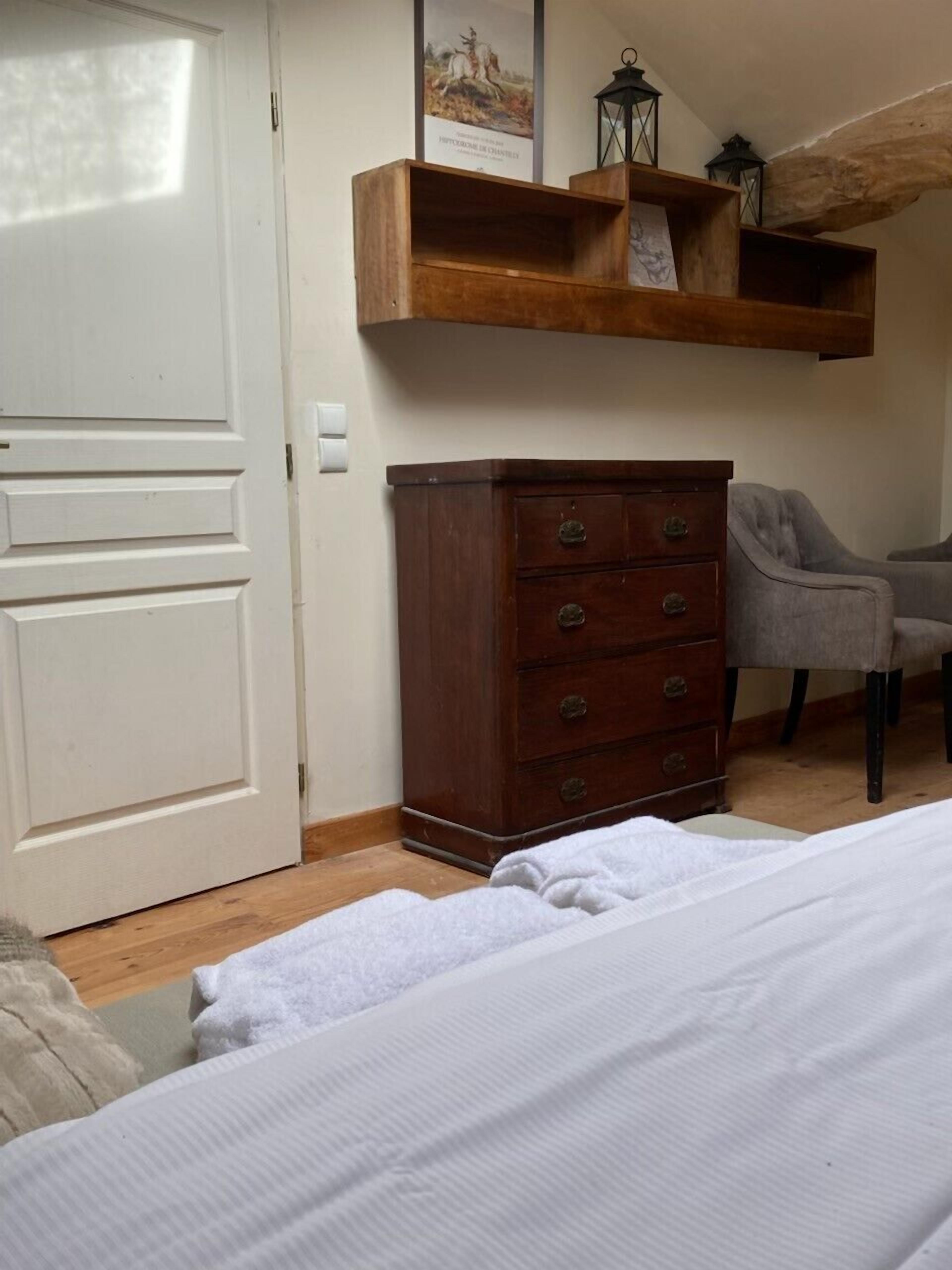 A bedroom with a wooden dresser, a chair, and a bed with white bedding.