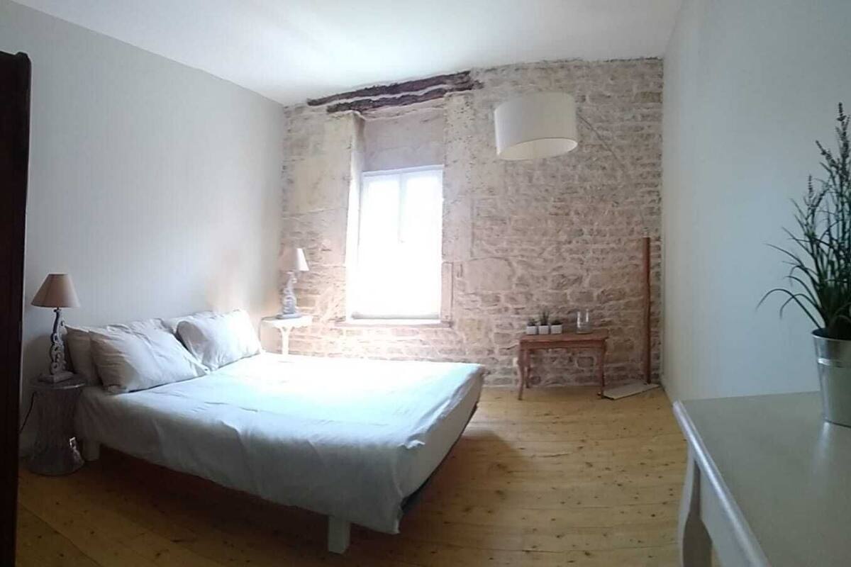 Un dormitorio con una cama, una mesita de noche, una lámpara, una planta en maceta y una pared de piedra.