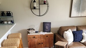 A cozy living room with a wooden floor, a brown leather sofa, a coffee table, and a dining area with wicker chairs. - Ground Floor Waterfront Condo! (Montgomery)