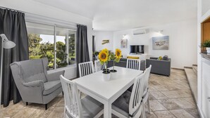 Un espace de vie moderne avec une table blanche, un fauteuil à motifs noir et blanc et un canapé gris. Deux tournesols en pot sont posés sur la table.